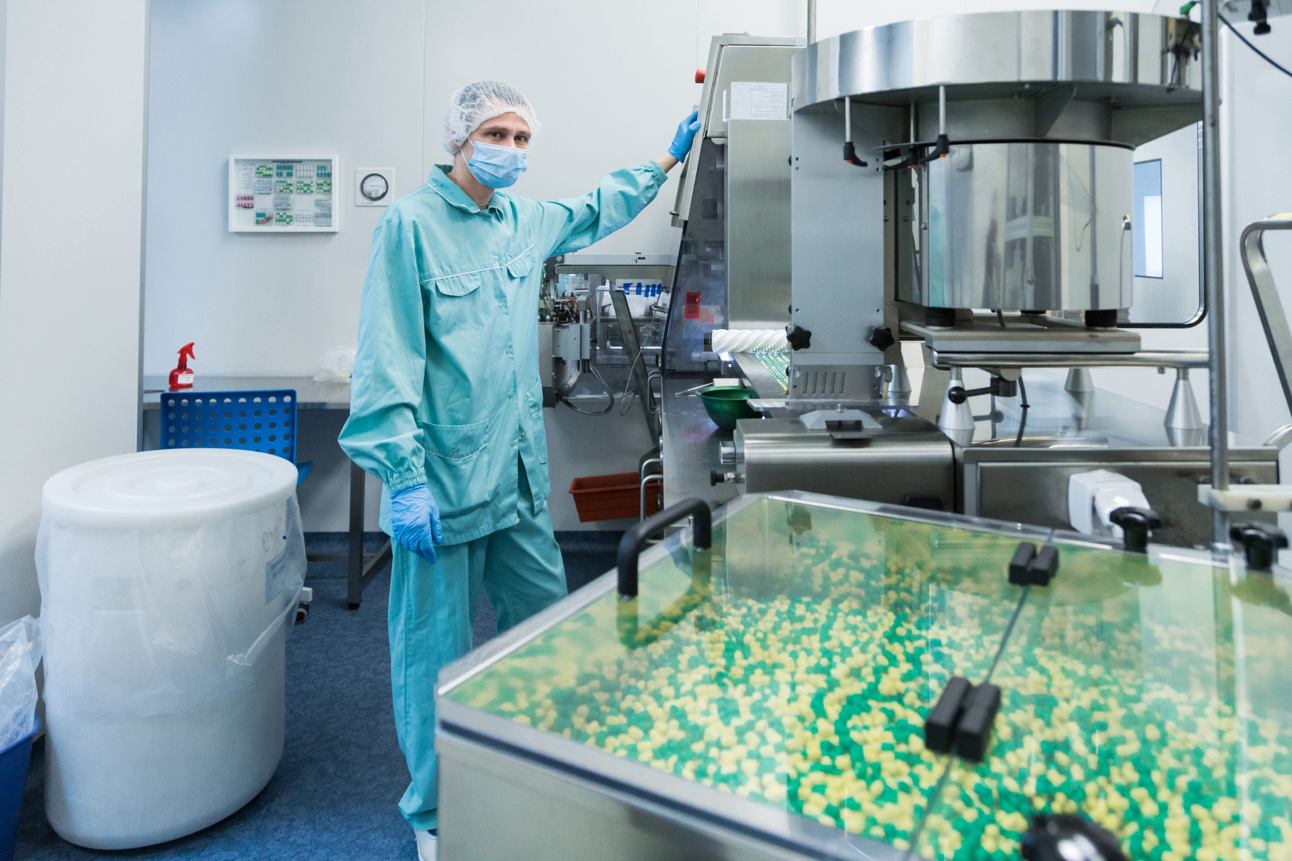 Pharmaceutical industry man worker in protective clothing operating production of tablets in sterile working conditions